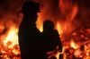 Silhouette of fireman carrying child with burning house beyond, British Columbia, Canada.