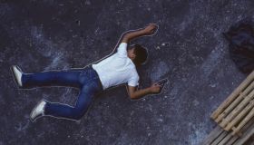 Man with gun lying on ground, chalk outline around him, elevated view