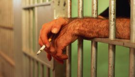 Man's hands poking through bars of jail cell, holding lit cigarette