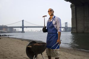 Young man cooking barbecue on beach, smiling
