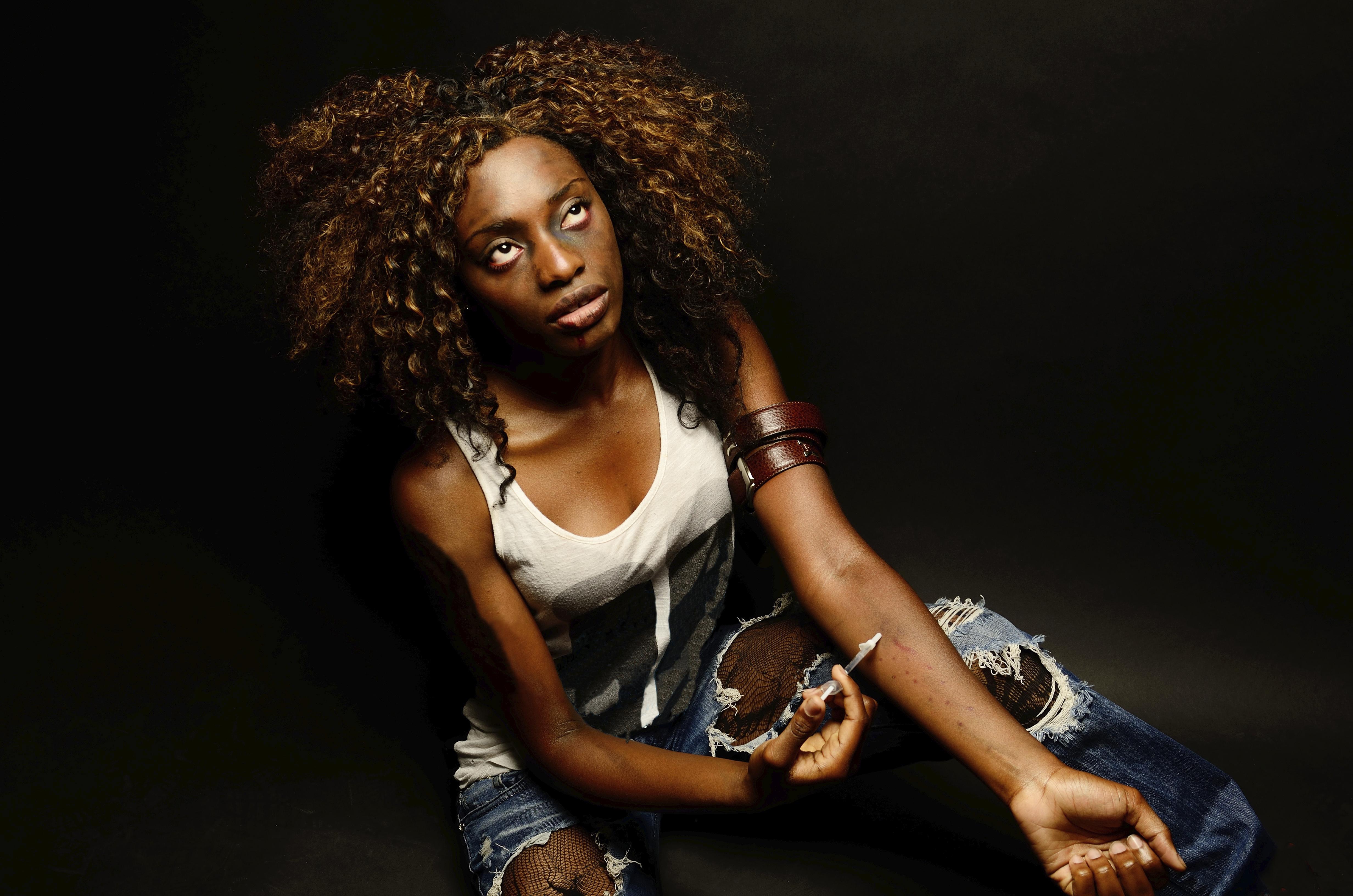 A young beautiful african american female poses as a track whore shooting up narcotics in this dark photo shoot against black