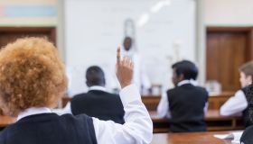 Waist up shot of African male teacher leading biology class, out of focus, students foregrounded with hands up, Cape Town, South Africa