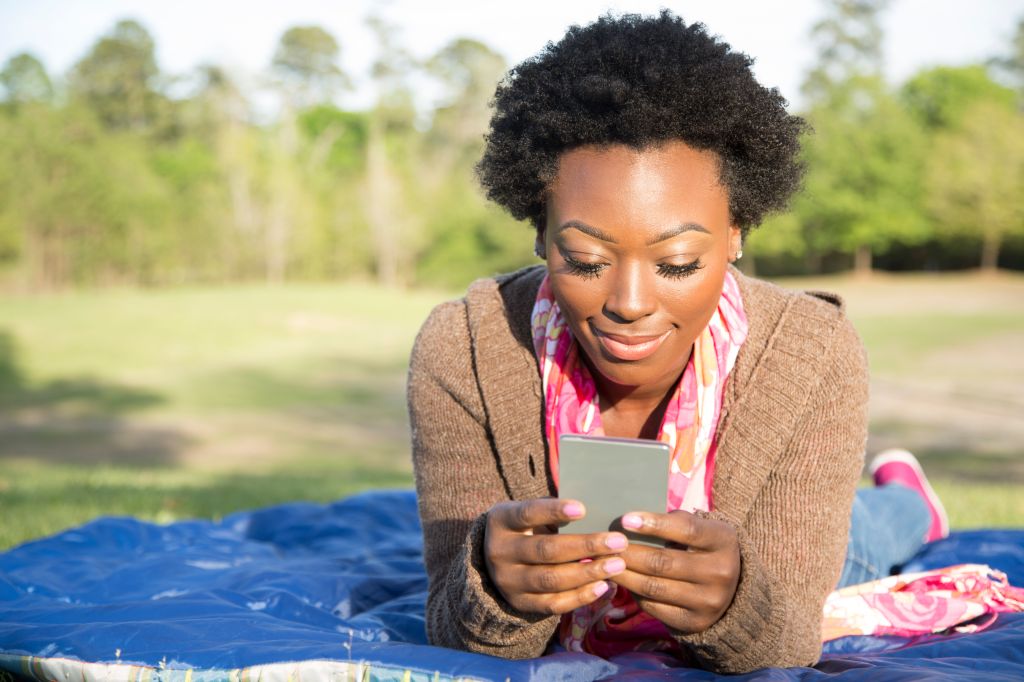 One African descent woman using cell phone outdoors in park.