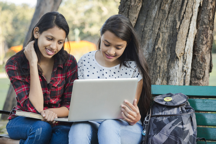 students with laptop sitting in park bench stock photo