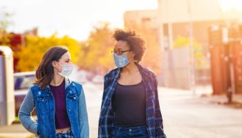 Two female friends walking down a Brooklyn alley wearing face masks