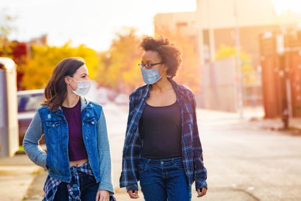 Two female friends walking down a Brooklyn alley wearing face masks