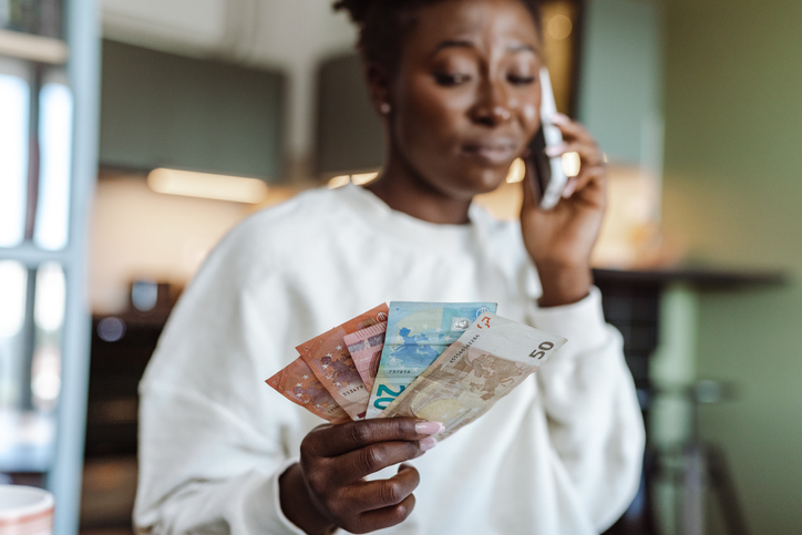 Worried African-American woman talking on the phone and holding money