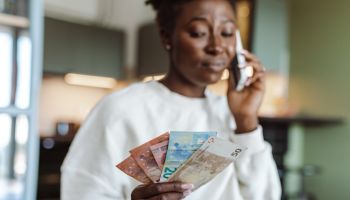 Worried African-American woman talking on the phone and holding money