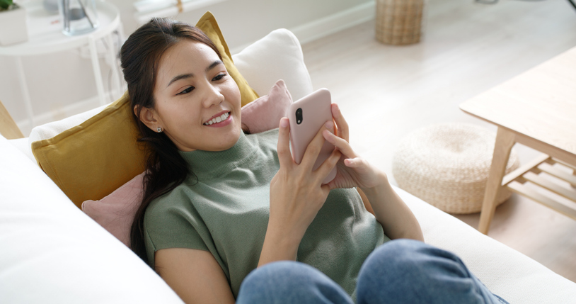 Young attractive beautiful casual asia female lady or student look at cellphone play social media IG reel tiktok app lying down at sofa couch living room feel relax comfort carefree at home apartment.