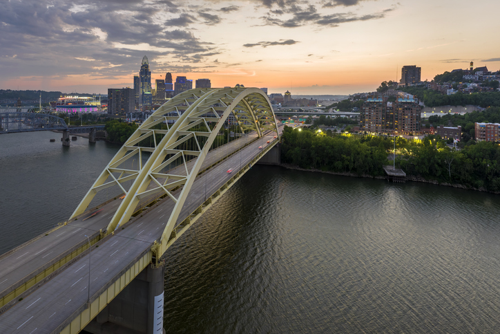 Cincinnati, Ohio with driving cars on Daniel Carter Beard Bridge highway near illuminated high skyscraper buildings in downtown district in USA. American city with business financial district at night