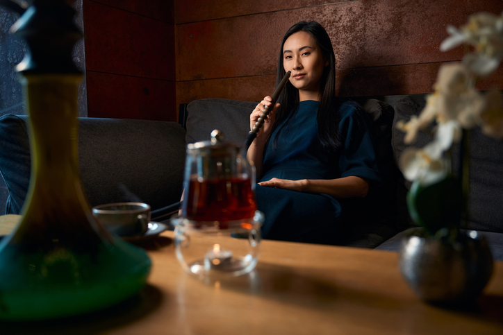 Asian flirty woman sitting at the table and smoking hookah