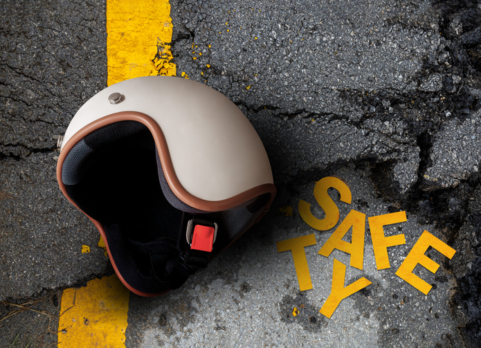 Motorcycle helmet on cracked asphalt road with scattered âSafetyâ letters. concept of road safety