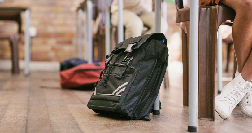 Children’s bag near desk in school, of students sitting in class. Backpack of kids studying, resting on table leg, in classroom learning environment. Pupil seated in homeroom, for basic education