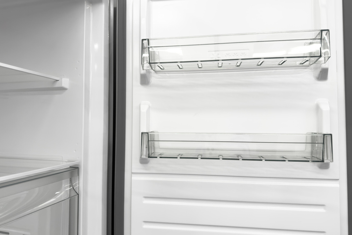 Clean empty white household refrigerator interior with clear plastic door shelves and crisper drawer