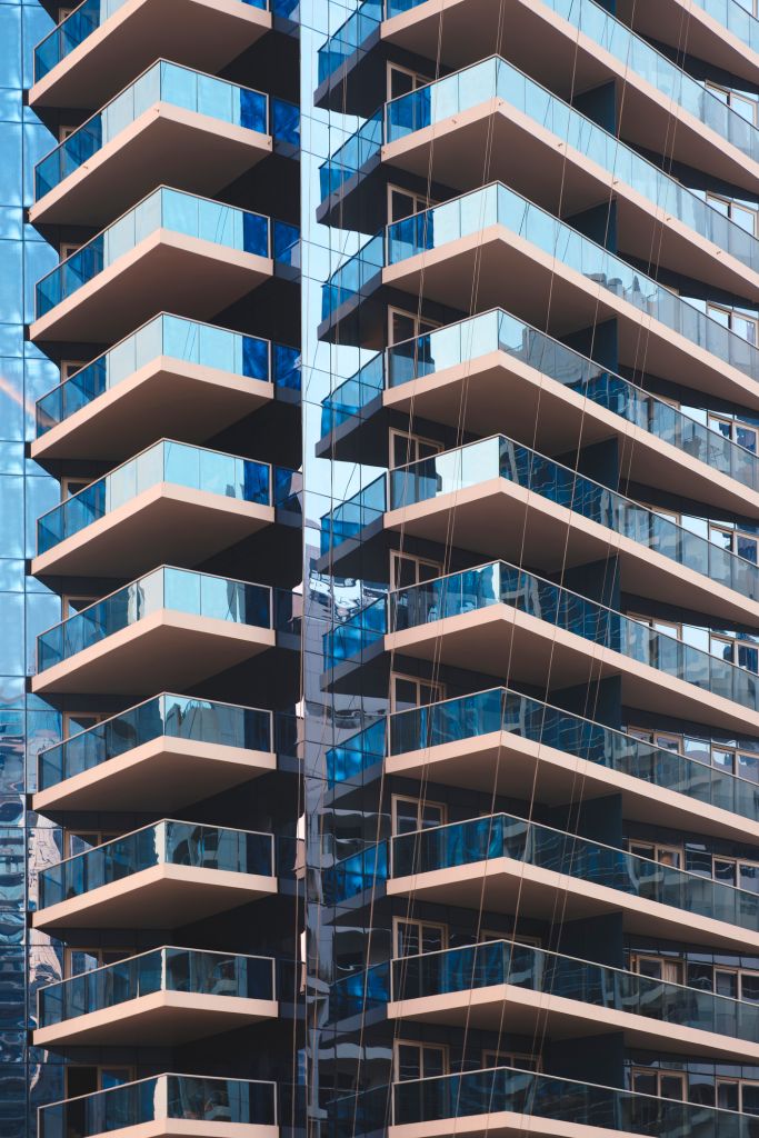 all modern apartment building with glass balconies and reflective windows. Sunlight highlights clean lines and urban architecture. Ideal for real estate, cityscape