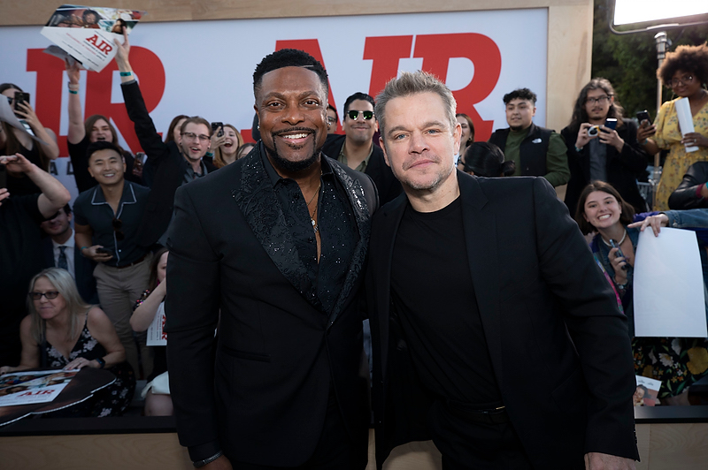 Two men, one Black and one white, smiling and posing together in front of a large "AIR" sign at a movie premiere event.