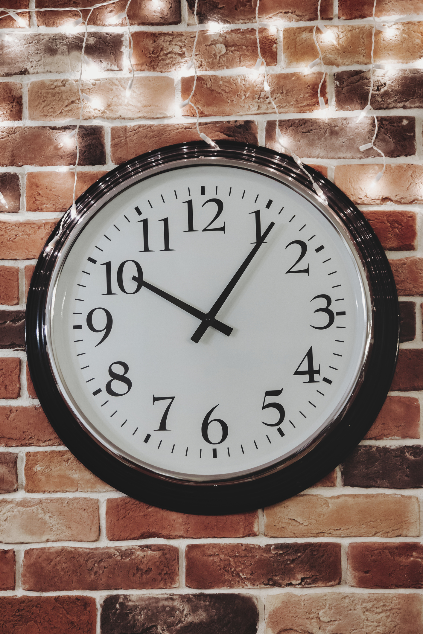 Wall Clock Against a Brick Wall With Fairy Lights Showing the Time as Ten O'clock