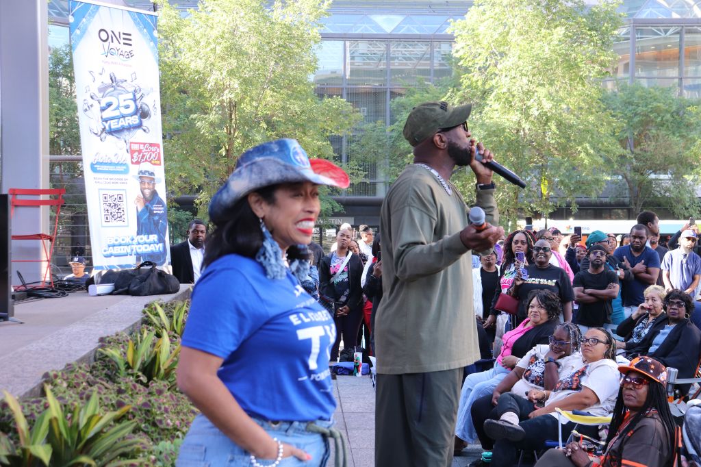 A crowd gathered in an outdoor setting, with a person speaking into a microphone and another person wearing a blue jersey with the number 7.