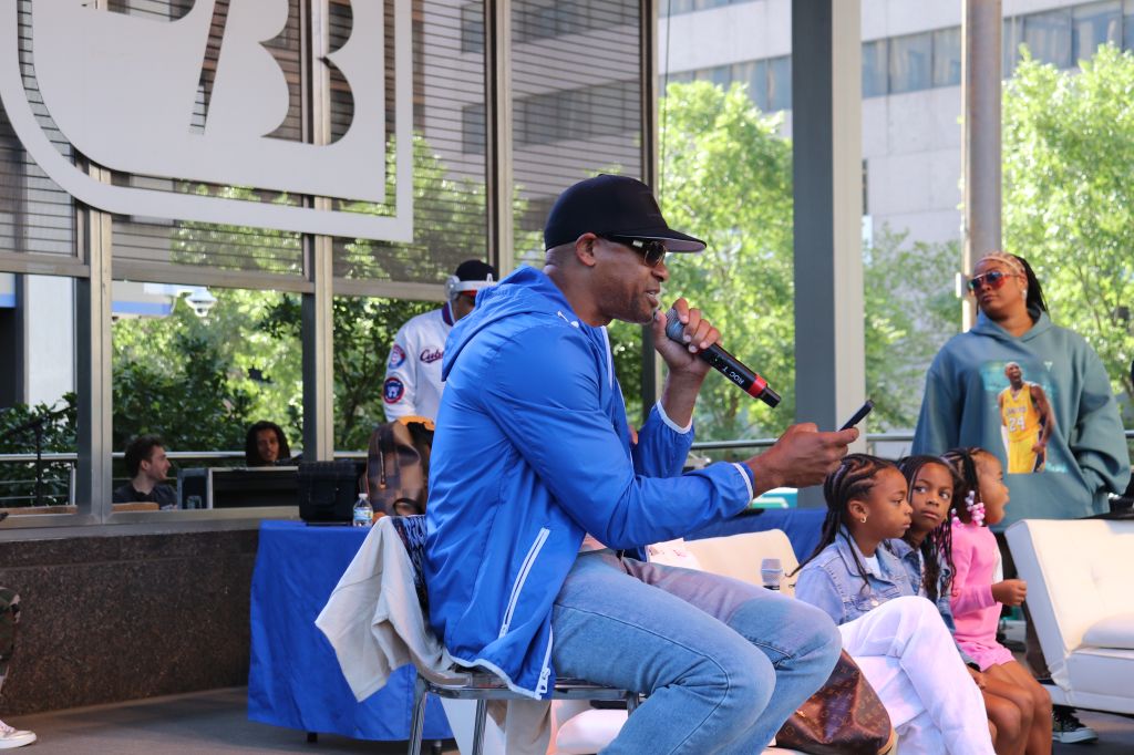 A man in a blue jacket performing on stage in front of a crowd, including children, at what appears to be an outdoor event or festival.