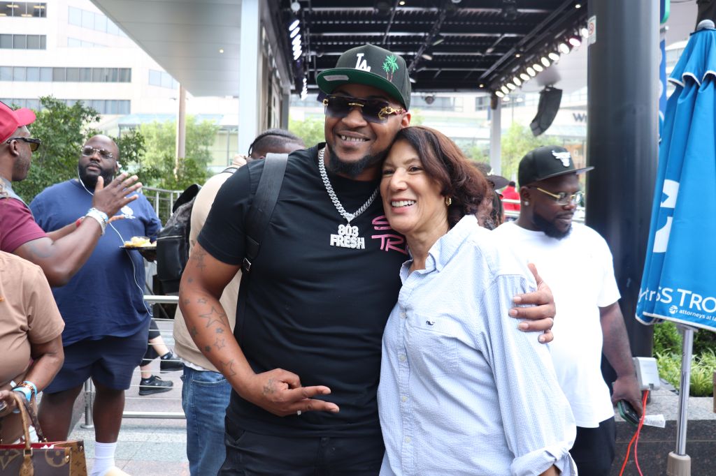 A smiling man wearing a black t-shirt with "Cali Fresh" printed on it, embracing a smiling woman in a white shirt.