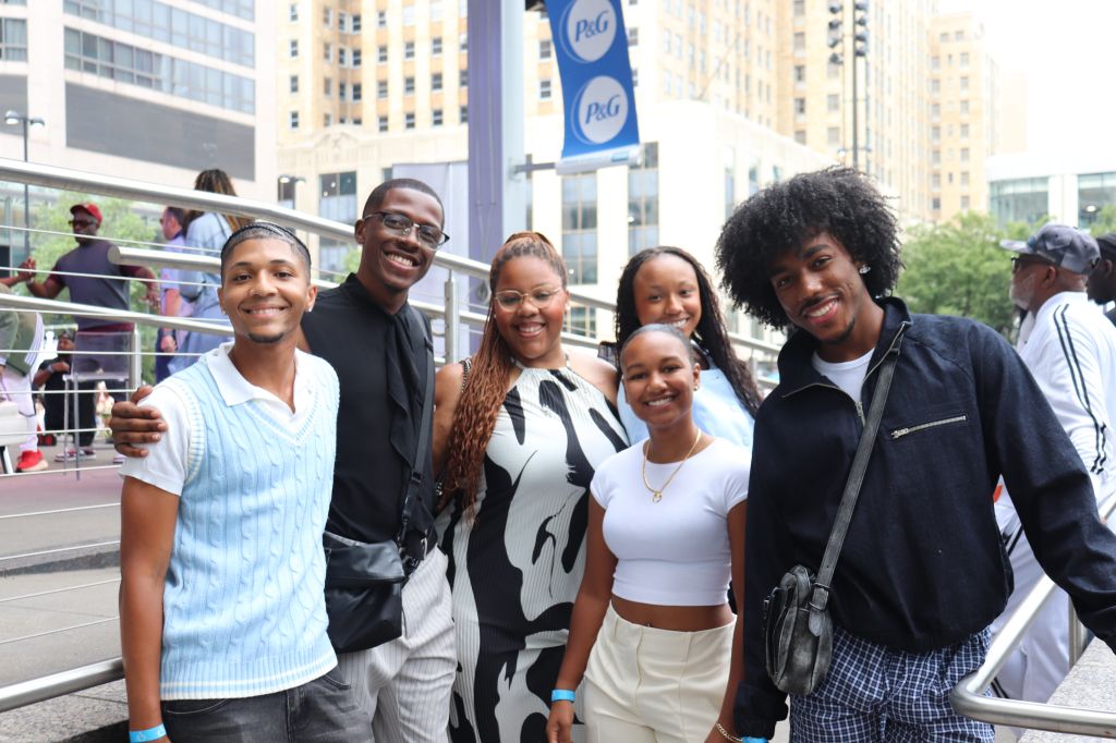 A group of smiling young people standing in front of P&G advertising banners in an urban setting.