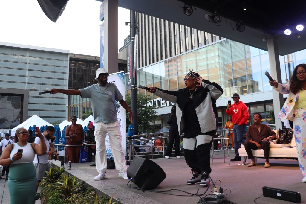 Two people performing on a stage in an urban setting, with a large glass building visible in the background.