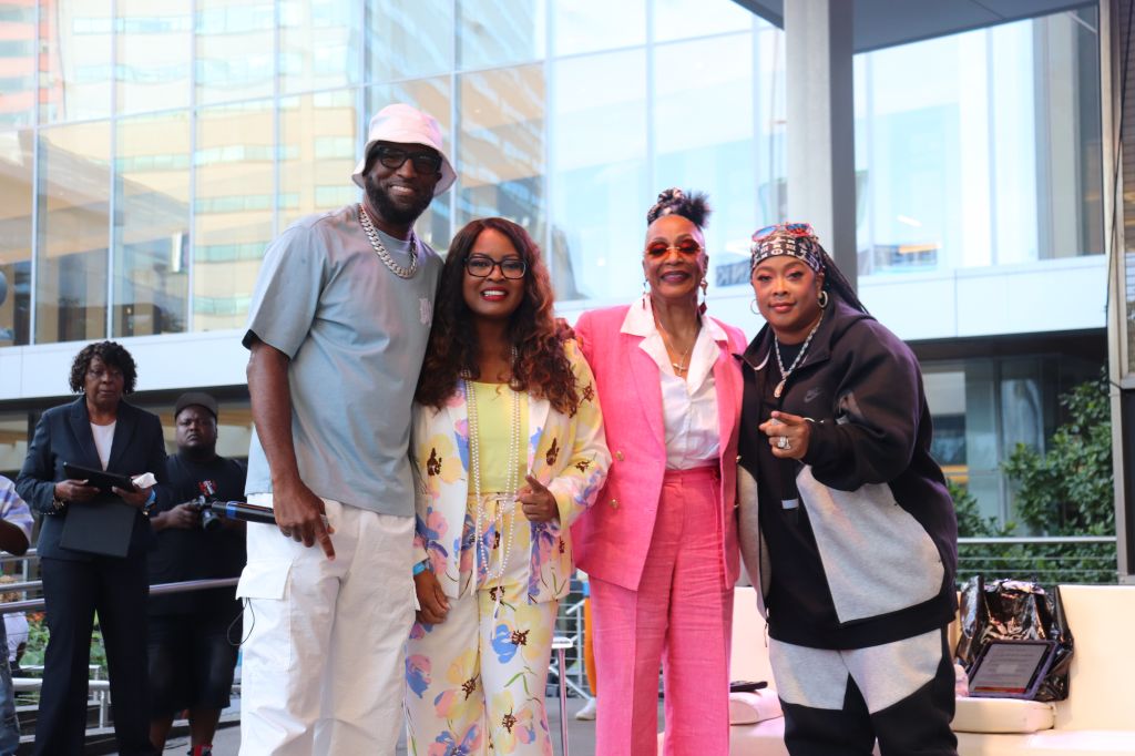 A group of four people, including two women and two men, standing together in a bright, modern setting. The women are wearing colorful, stylish outfits, and the men are wearing casual clothing. They appear to be posing for a photograph.
