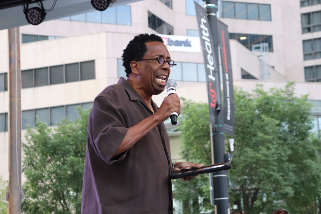 A man speaking into a microphone at an outdoor event, with a bank logo visible in the background.
