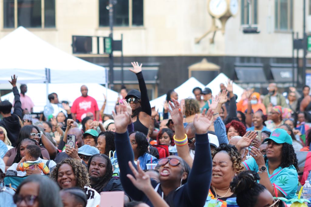 A large crowd of people with their hands raised, celebrating and cheering at an outdoor event.