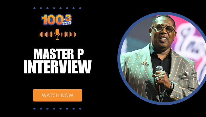 A man wearing sunglasses and a striped suit speaking into a microphone on a stage, with "100.3" and "Master P Interview" text overlaid.