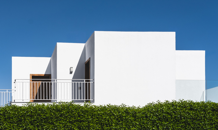 Modern white villa with minimalist design with greenery under clear blue skies.