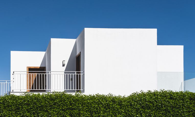 Modern white villa with minimalist design with greenery under clear blue skies.